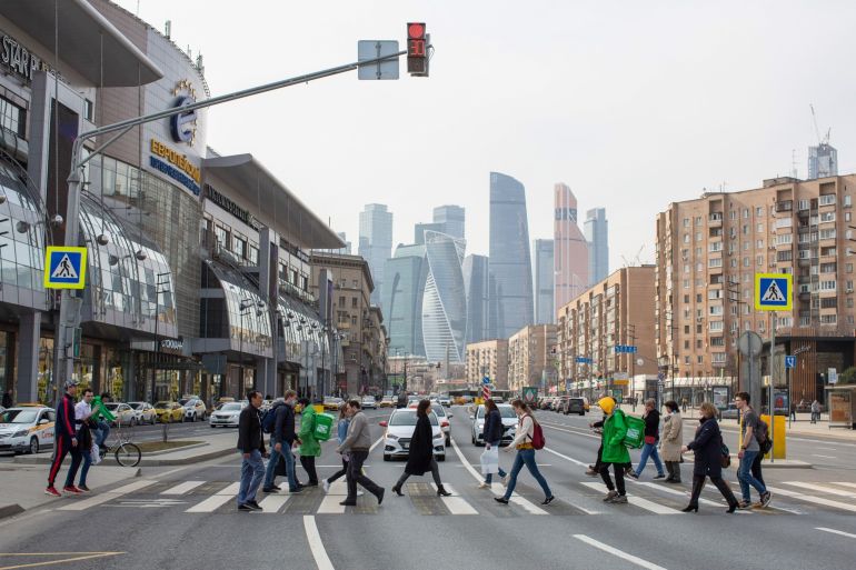 Pedestrians cross a street in front of skyscraper office buildings situated in the Moscow International Business Center (MIBC), also known as 'Moscow City,' in Moscow, Russia