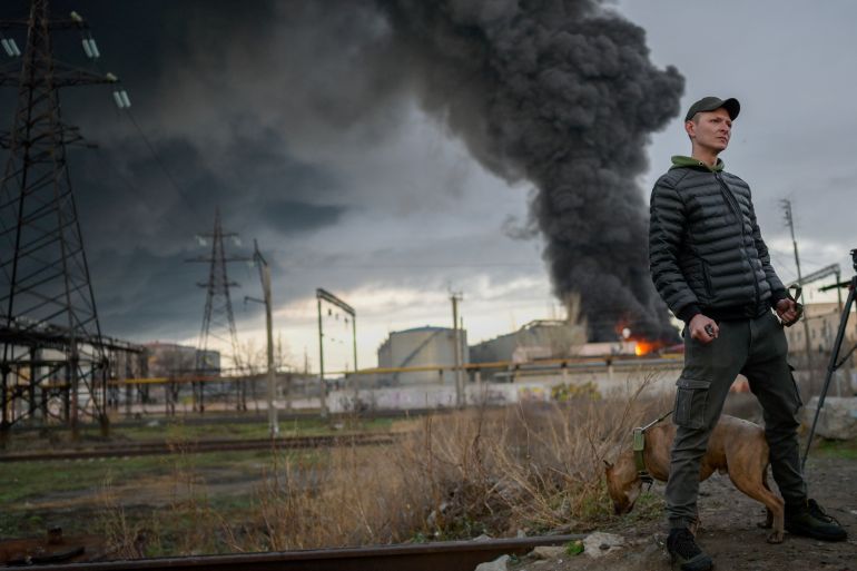 A man stands with his dog as smoke rises after an attack by Russian army in Odesa.