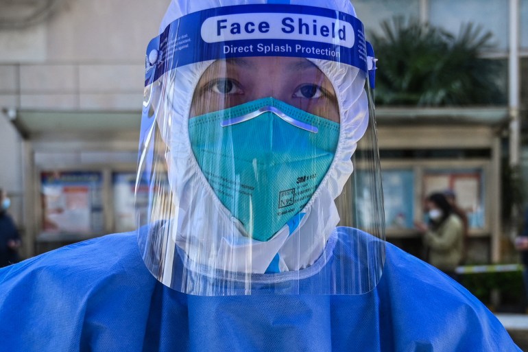A healthworker in China in full PPE including mask, shield and hooded gown prepares to take a swab test from a Shanghai resident