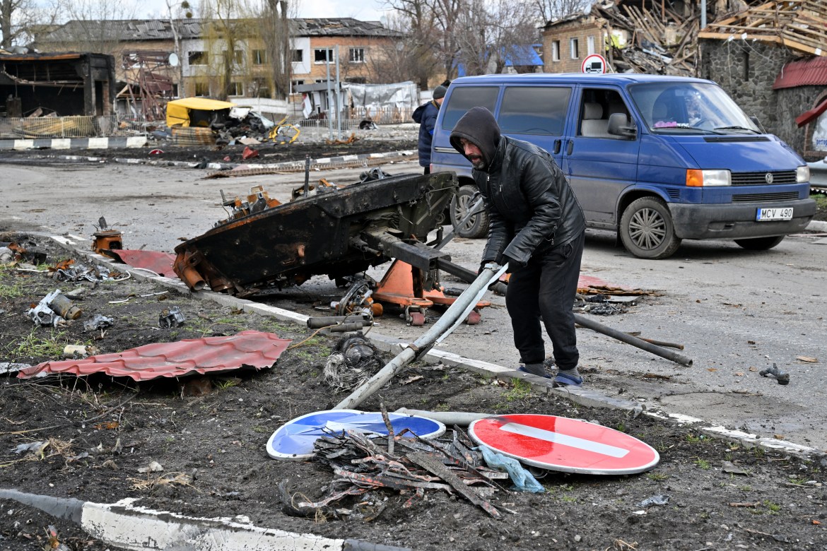 A man removes trash near the rest of a destroyed Russian armoured personnel