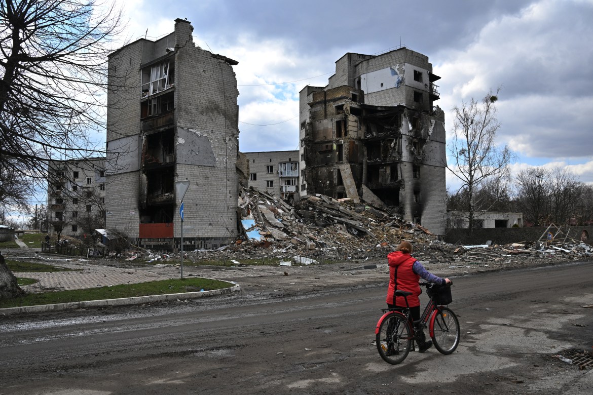 A woman carries her bicycle past destroyed buildings in the town of