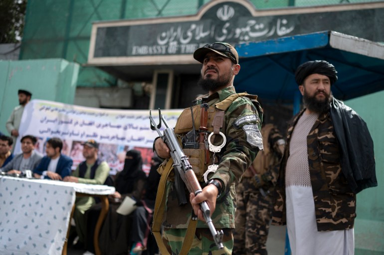 Taliban fighters stand guard as Afghan protestors take part in a protest against the alleged published reports of harassment of Afghan refugees in Iran, in front of the Iranian embassy in Kabul