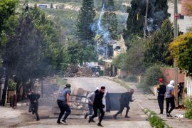 Palestinian protesters run across a street as plumes of tear gas fired by Israeli troops rises into the air near Homesh, in the village of Burqa in the north of the occupied West Bank on April 19, 2022.