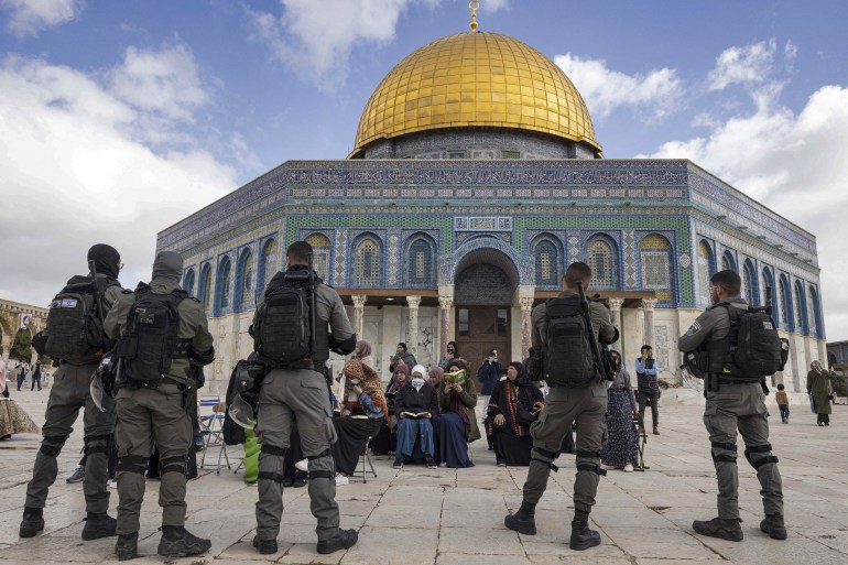 Israeli policemen stand in front of Muslim women praying with the Dome of the Rock in the backdrop