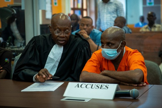 Ousman Yaouba sits in the court room next to his lawyer wearing an orange prison uniform.