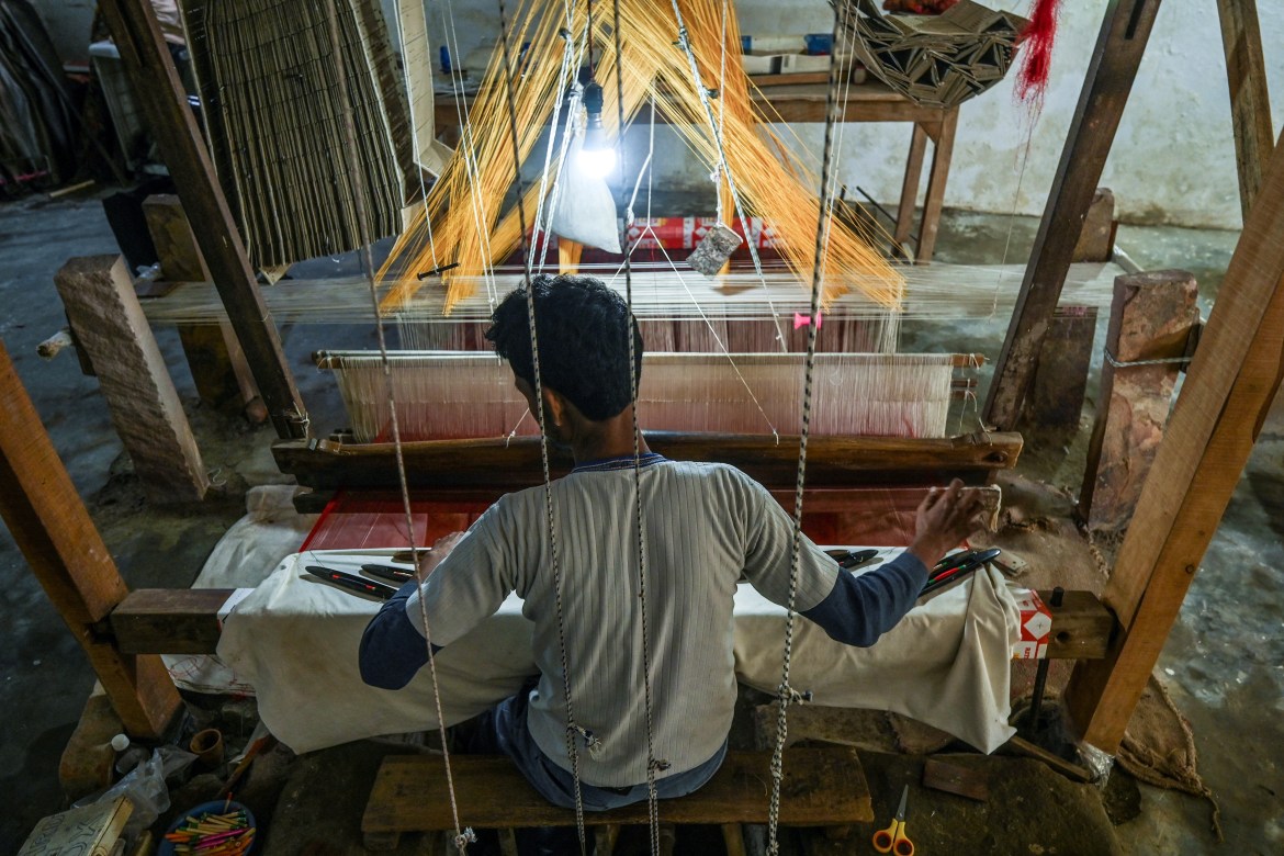 a worker uses a hand loom to weave a traditional Banarasi silk sari