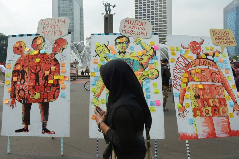 An Indonesian woman in a black headscarf walks past murals protesting against sexual abuse during a Jakarta protest