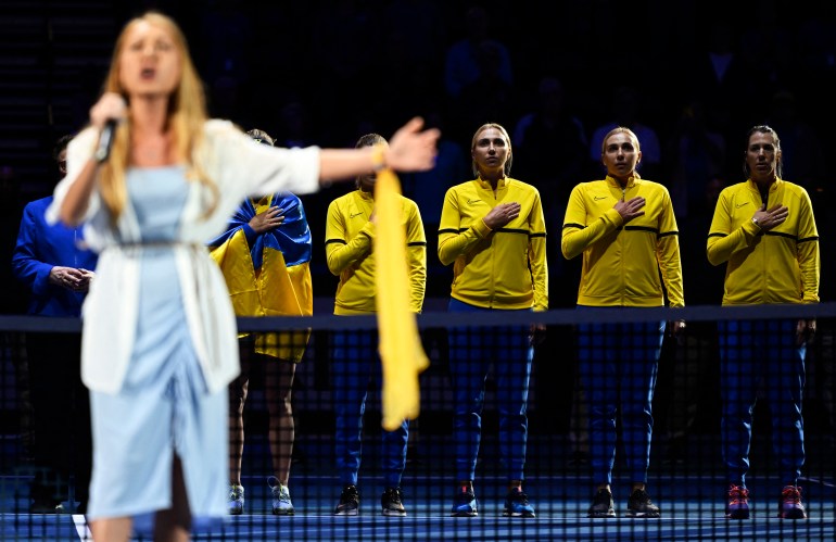 The Ukrainian team listens to Yuliia Kashirets sing the Ukrainian national anthem during the opening ceremonies for the Billie Jean Cup qualifier