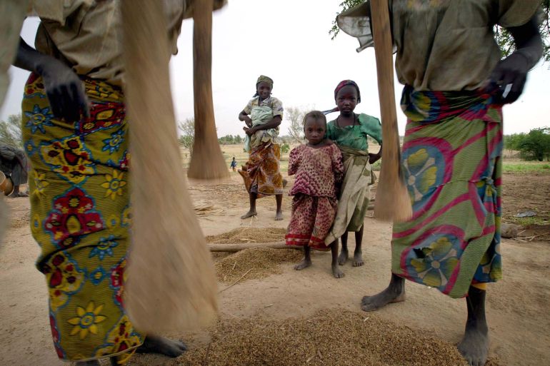 Children watch as women pound millet at a village in southern Niger