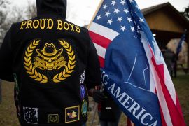 A member of the Proud Boys at a rally with the US flag emblazoned with a partial hidden political message.