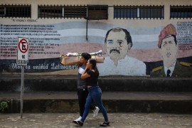 People walk by a mural showing Daniel Ortega and Hugo Chavez