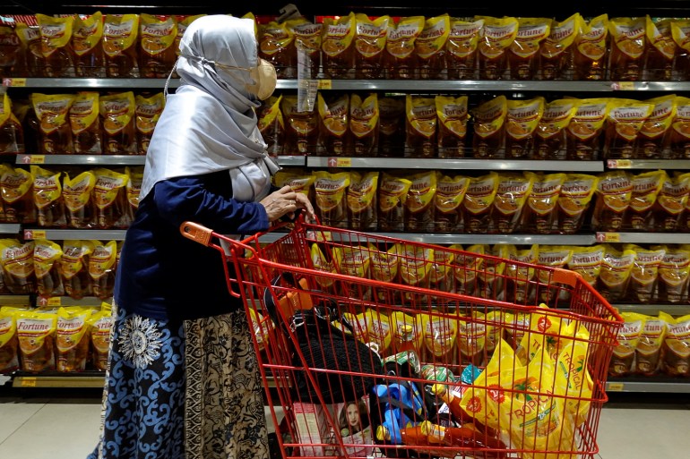 A woman in Jakarta pushes her trolley down a supermarket aisle stocked with cooking oil made from palm oil