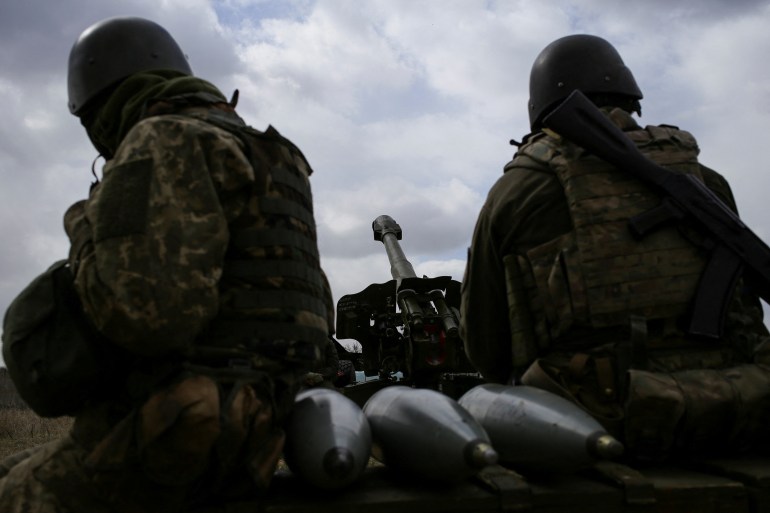 Members of Ukrainian volunteer corps sit next to a howitzer