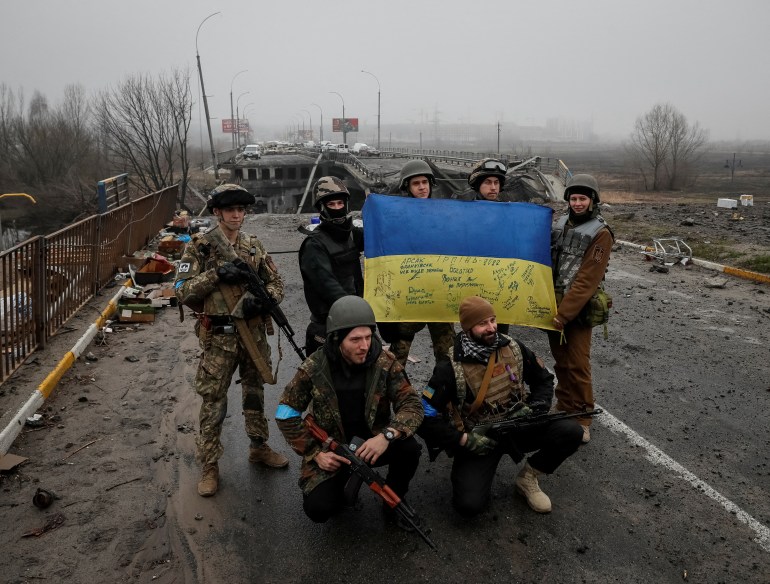 Ukrainian servicemen pose for a picture near a destroyed bridge as Russia's invasion of Ukraine continues, in the town of Irpin outside Kyiv
