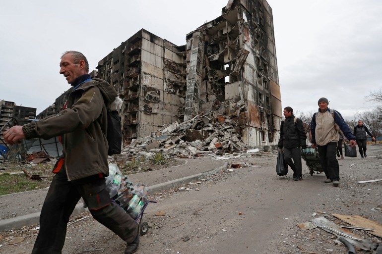 Local residents walk past a building destroyed during Ukraine-Russia conflict in the southern port city of Mariupol,