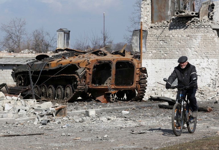 A local resident rides a bicycle past a charred armoured vehicle during Ukraine-Russia conflict in the separatist-controlled town of Volnovakha in the Donetsk region