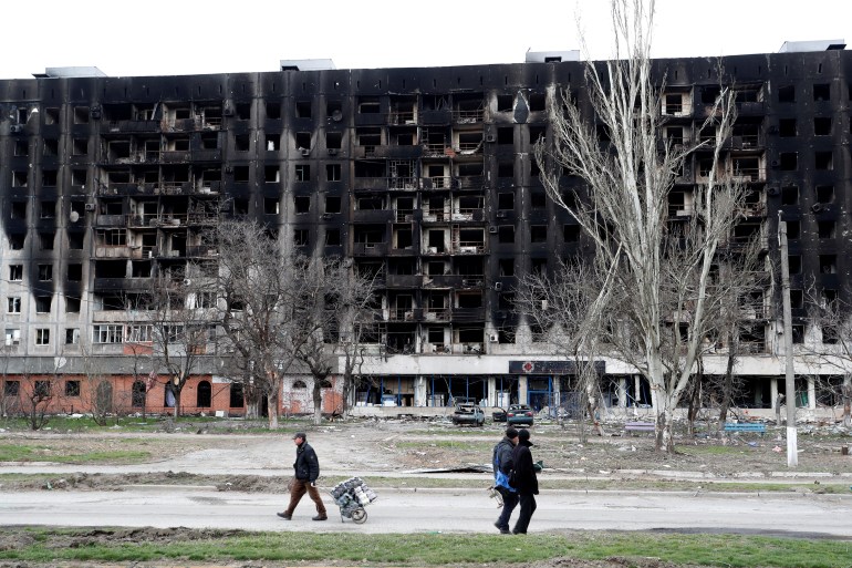 Local residents walk past a burned building during Ukraine-Russia conflict in the southern port city of Mariupol