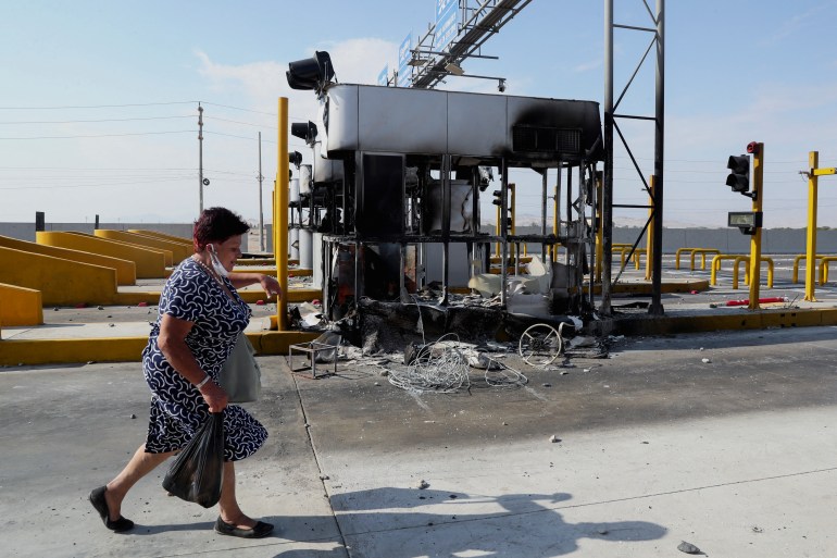 A woman walks past burned toll booths on a highway to Lima during a national transportation strike against gas prices and toll road rates, in Ica, Peru April 4, 2022.