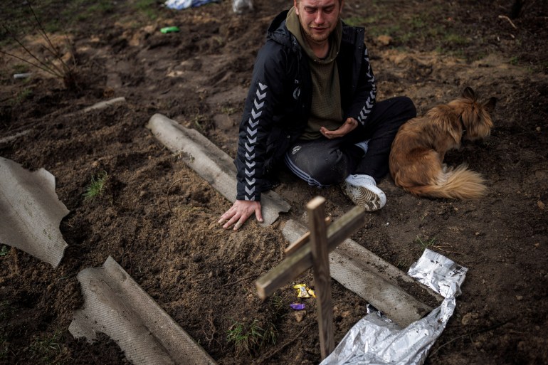 A man is seen mourning next to a grave in Bucha