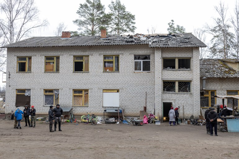 La gente se para frente a una escuela dañada, mientras continúa la invasión rusa de Ucrania, en el pueblo de Yahidne, cerca de Chernihiv.