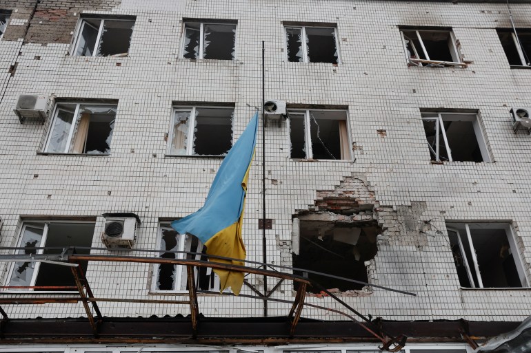 A Ukrainian national flag flutters on a building damaged by shelling