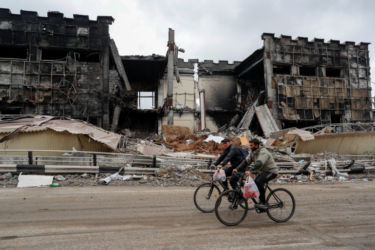Men ride bicycles past a building destroyed during Ukraine-Russia conflict