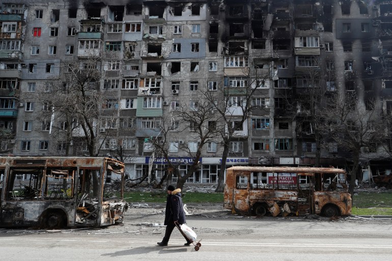 A local resident walks along a street past burnt out buses during Ukraine-Russia conflict in the southern port city of Mariupol.