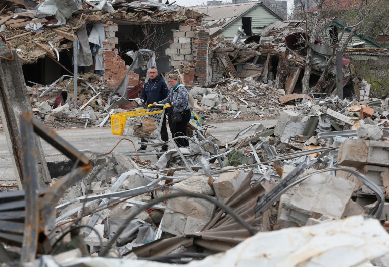 Moradores locais passam por prédios destruídos durante o conflito Ucrânia-Rússia na cidade portuária de Mariupol, no sul da Ucrânia