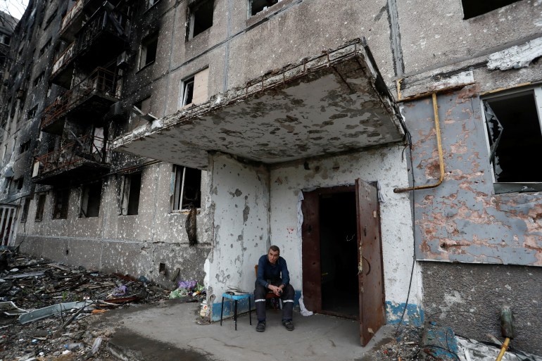 A resident sits on a bench in front of a heavily-damaged building in Mariupol, Ukraine.