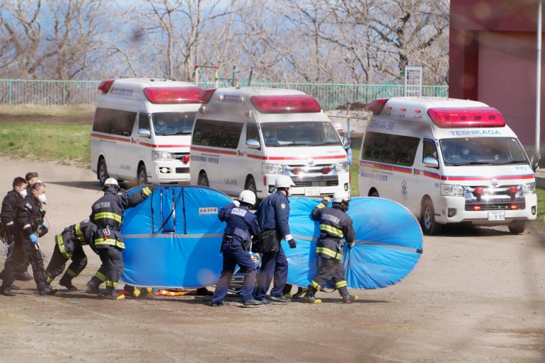 Firefighters and police officers transport rescued people from the missing tour boat Kazu 1 from Japanese Self-Defence Force's helicopters in Shari, Hokkaido Prefecture