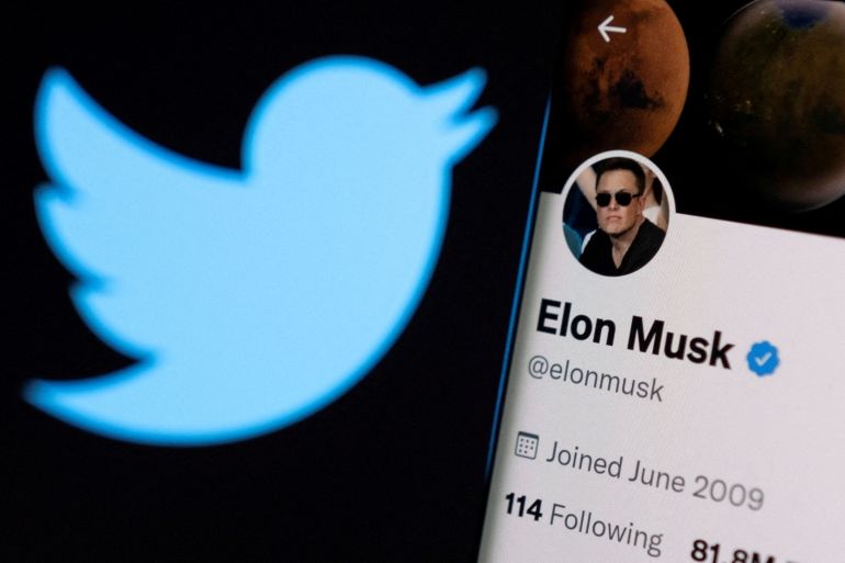 Elon Musk's twitter account is seen on a smartphone in front of the Twitter logo.