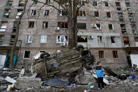 A boy stands next to a wrecked vehicle in front of an apartment building damaged during Ukraine-Russia conflict in the southern port city of Mariupol