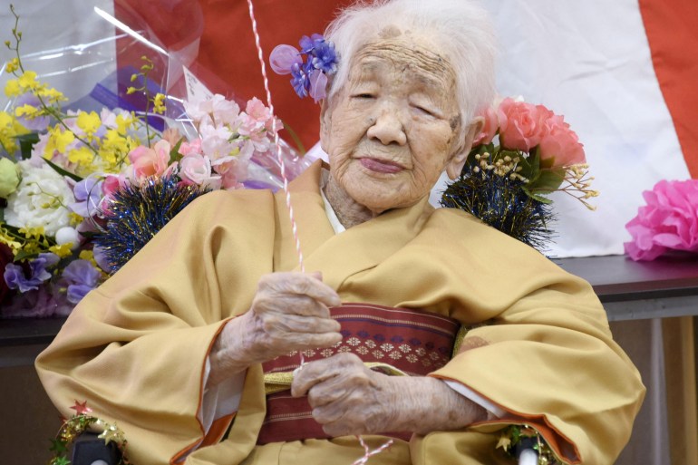 Kane Tanaka, vestida con un kimono tradicional amarillo y rodeada de flores, en la foto celebrando su 117 cumpleaños