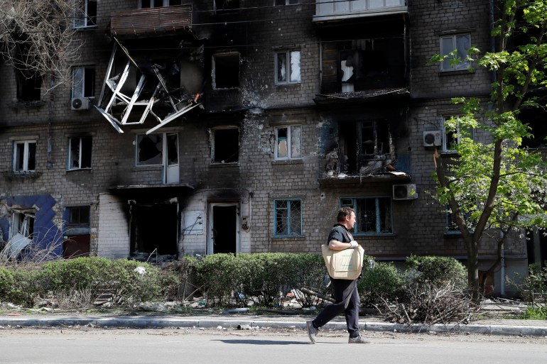 A man walks past a residential building, which was damaged during Ukraine-Russia conflict in the southern port city of Mariupol.