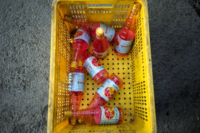 Eight bottles of Rooh Afza sit haphazardly in a yellow crate on the ground, ready to be prepared at a charitable food distribution site.