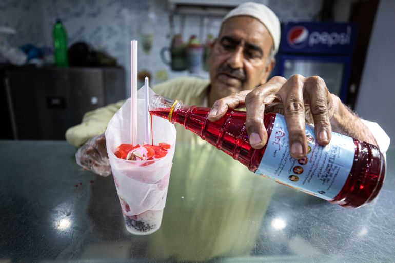 Photo of a man drizzling Rooh Afza on top of a drink made by blending milk, jelly, tapioca balls and pieces of fruit