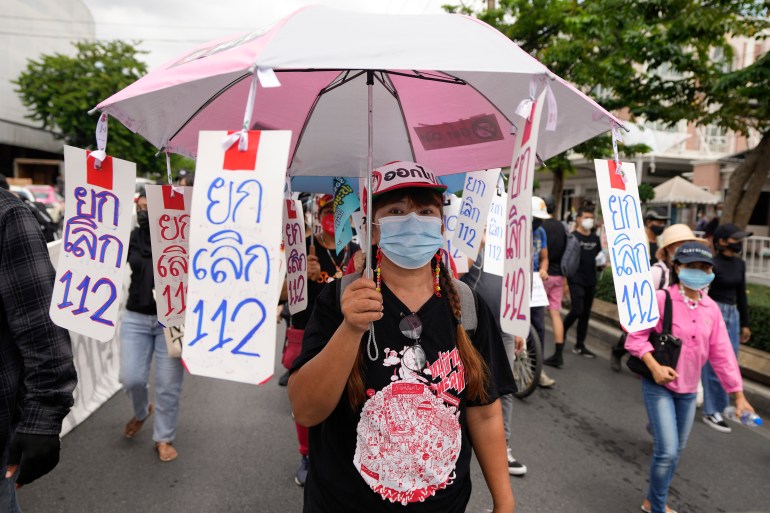 Eine Frau trägt einen Regenschirm, der mit Plakaten geschmückt ist, die die Aufhebung der königlichen Verleumdungsgesetze Thailands, bekannt als 112, fordern.