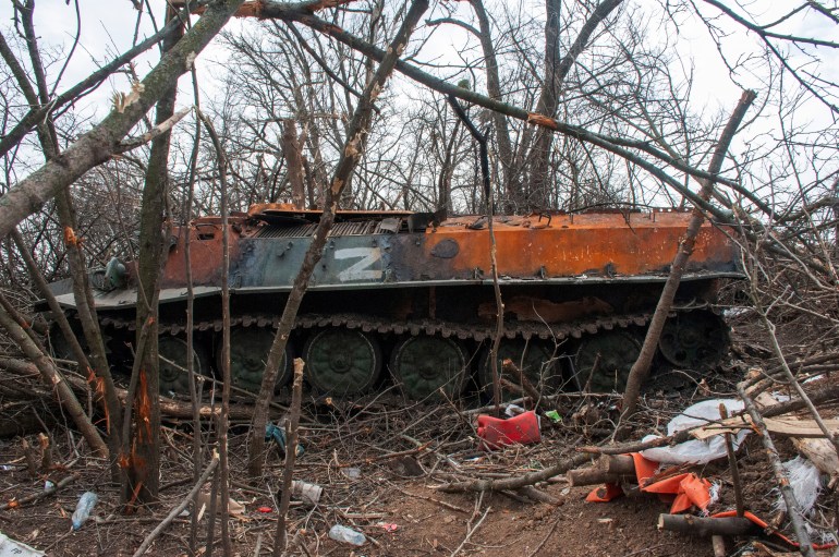 An armored vehicle sits destroyed in a field among bare trees near the village of Malaya Rohan