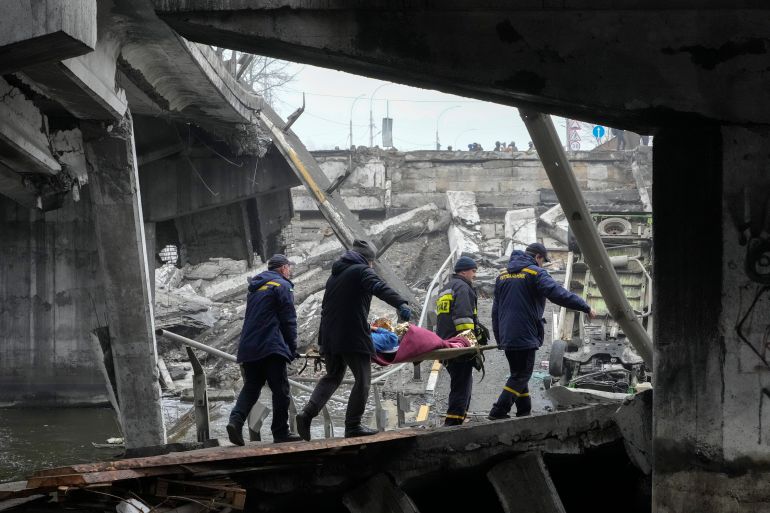 Rescue workers evacuate an elderly woman among destroyed buildings in Irpin