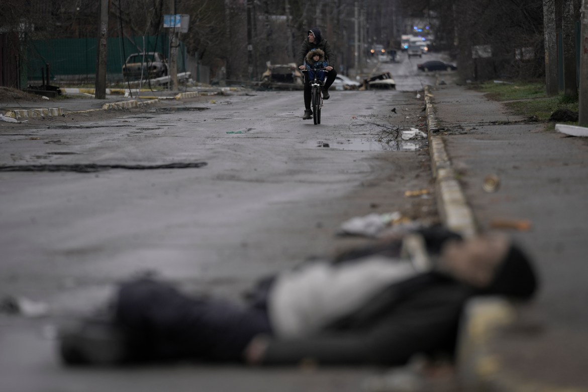 A man and child on a bicycle come across the body of a civilian lying on a street
