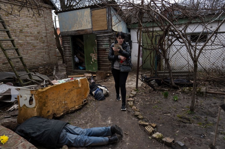 A woman is seen walking next to the corpses of her husband and her brother in Bucha