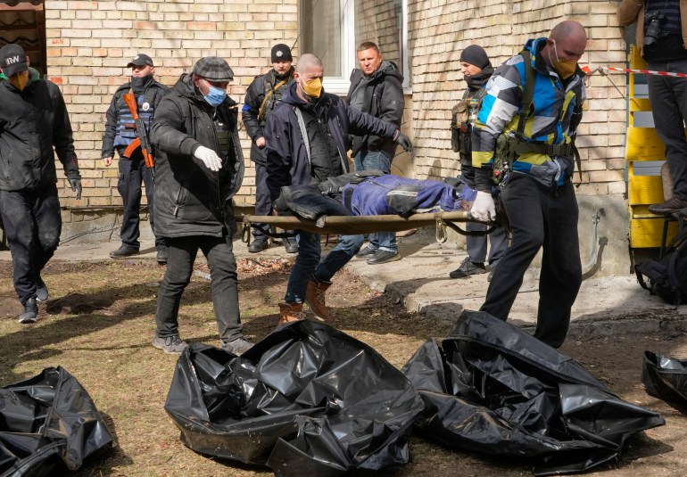 Ukrainians bring out the body of one of dozens of civilians allegedly killed by Russian troops in Bucha, Ukraine, with more bodies covered in black plastic lying on the ground in front of them.