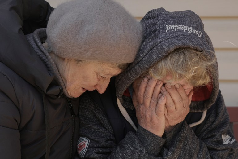 A neighbour comforts a distraught Natalya as she sobs and covers her face with her hands after her husband and nephew were killed in Bucha