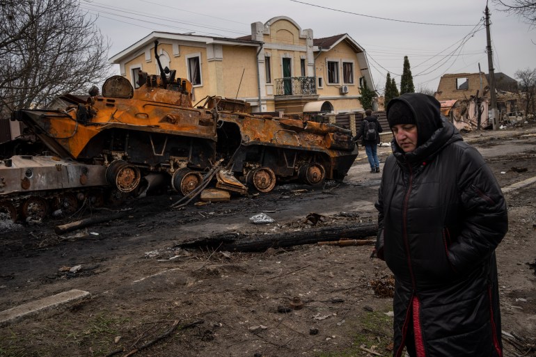 A woman walks next to a destroyed Russian armor vehicle in Bucha