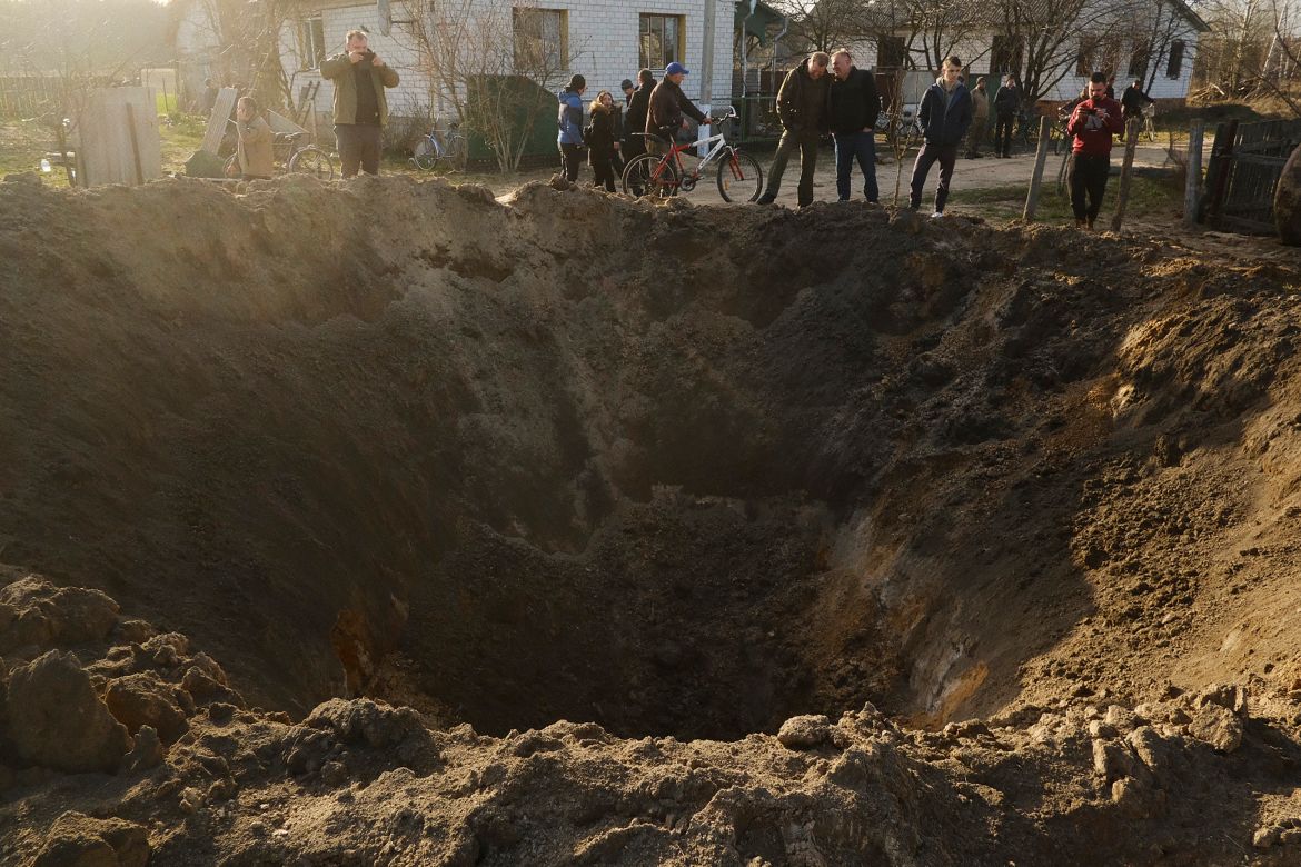 People look at a crater of an explosion in a village of Horodnya, Chernihiv region
