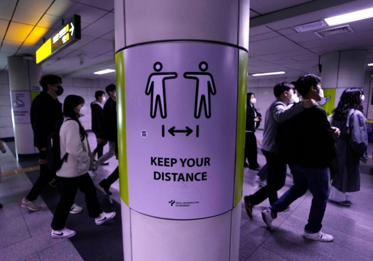 People wearing face masks pass by a poster reminding precautions against the coronavirus at a subway station in Seoul,