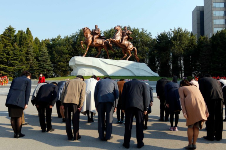 A small group of North Koreans bow to the bronze-colored statues of Kim Il Sung and Kim Jong Il on horseback