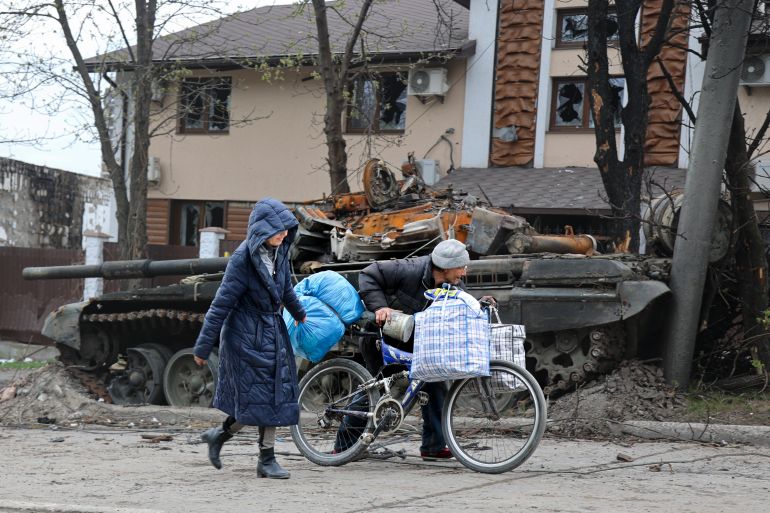 Local civilians walk past a tank destroyed during heavy fighting in an area controlled by Russian-backed separatist forces in Mariupol, Ukraine, Tuesday, April 19, 2022.