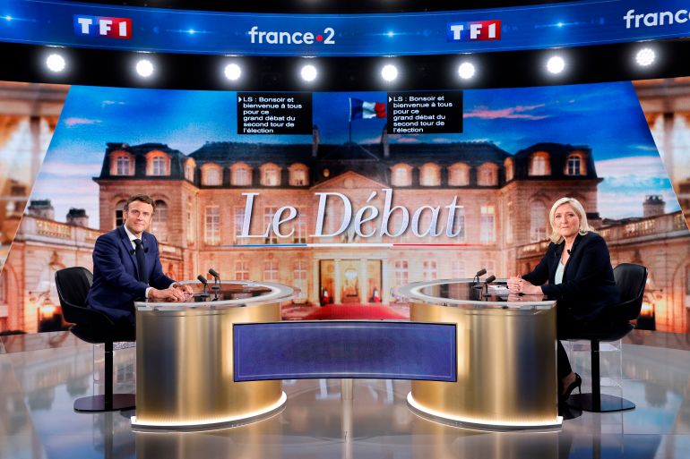 Emmanuel Macron and Marine Le Pen face each other from golden coloured tables against a picture of the Elysee Palace and the words 'Le Debat' ahead of the candidates single debate before Sunday's election.
