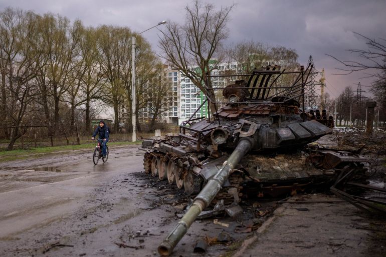 A man rides his bicycle next to a destroyed Russian tank in Chernihiv, Ukraine.